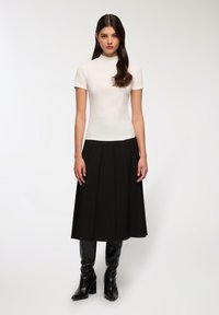 Biała, dopasowana bluzka z krótkim rękawem i wysokim dekoltem, w połączeniu z czarną plisowaną spódnicą midi i czarnymi wysokimi botkami. Gładka struktura na całej powierzchni.