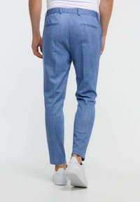 Pantalones ajustados de color azul claro, confeccionados en una mezcla de algodón. Cuentan con dos bolsillos traseros y piernas afiladas, combinados con zapatos blancos.
