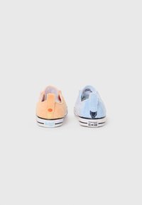 Chaussures en peluche orange et bleue à enfiler avec des textures contrastées. Chacune dispose d'une boucle à l'arrière et de détails de marque sur le talon.
