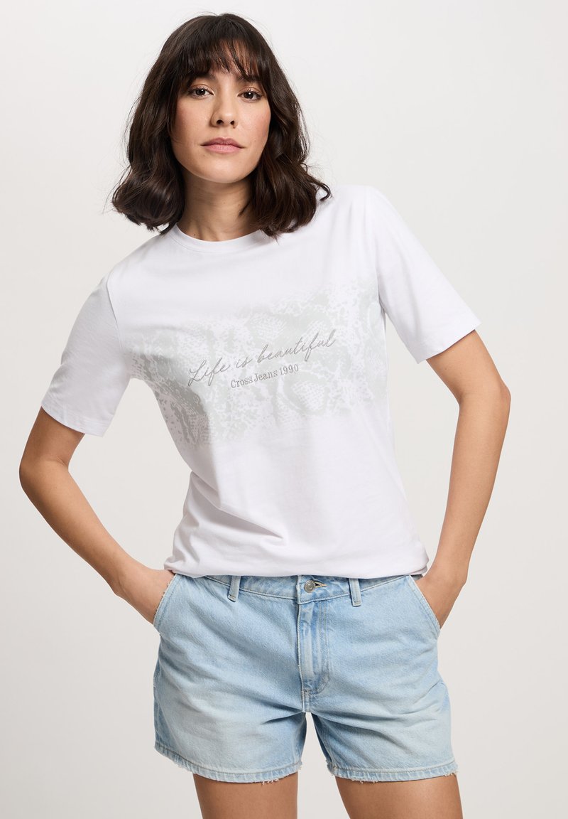 Biała bawełniana koszulka z krótkim rękawem z szarym napisem „Życie jest piękne” oraz jasnoniebieskie szorty dżinsowe z postrzępionymi brzegami.