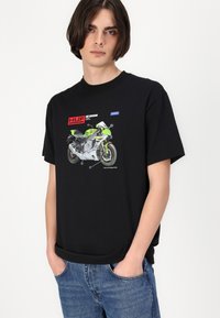 Zwarte katoenen t-shirt met een graphic van een groene motor, met tekstlabels en een ronde halsontwerp. Heeft een relaxte pasvorm rondom het lichaam.