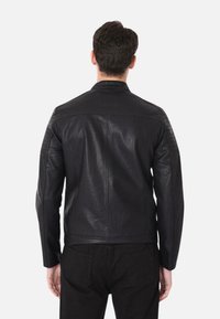 Giacca da moto in pelle nera con dettagli trapuntati sulle spalle, design aderente e superficie liscia, mostrata dal retro.