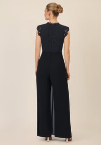 Mono navy con parte superior de encaje, escote con forma de ondas y diseño de pierna ancha. Presenta una espalda descubierta con una cremallera oculta y aberturas laterales.