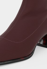 Близък план на текстурирана тъмнокафява обувка с ток, с видими шевове и черна подметка.