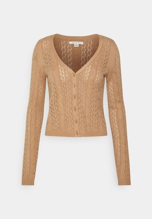 Béžový pletený kardigan s véčkovým výstřihem, dlouhými rukávy a zavíráním na knoflíky. Má vzor s průstřihy a žebrovaný lem.