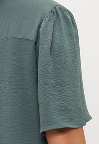 Σαλοπέτα κοντό μανίκι σε απαλή απόχρωση τιρκουάζ. Το ύφασμα διαθέτει υφή με κυματιστή επιφάνεια, απλό λαιμόκοψη και ίσιο στρίφωμα.