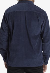 Navy corduroy shirt with vertical ribbed texture, buttoned cuffs, and a curved hem. Features a classic collar and plain back design.