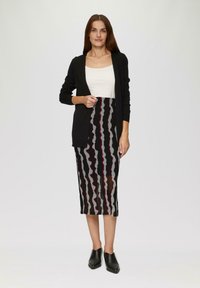Cardigan noir sur un top blanc, associé à une jupe transparente avec des rayures ondulées noires, grises et maron. Bottines noires.