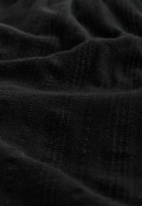 Schwarzer, strukturierter Stoff mit dezenten vertikalen Streifen, der eine weiche, leicht erhabene Oberfläche und einen glatten Fall aufweist.