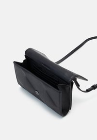 Černá koženková crossbody taška s prošívaným designem, přední klopnou, uzavíráním na patentku a několika sloty na karty uvnitř.