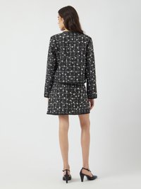 Giacca da abito in tweed nero e bianco con dettagli floreali, abbinata a una gonna coordinata. Le scarpe nere con tacco completano l'outfit.