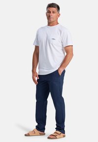 Camiseta de algodón blanca con un bolsillo en el pecho, pantalones navy y sandalias beige con un diseño de doble tira. Un conjunto simple y casual.