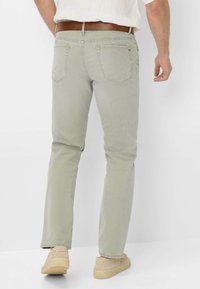 Pantaloni dritti verde chiaro realizzati in un tessuto morbido. Presentano tasche posteriori e una cintura in pelle marrone. Calzature casual visibili.