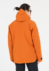 Orange vandtæt jakke med hætte, der har en glat tekstur og en justerbar pasform. Inkluderer sorte velcro-detaljer på ærmerne.