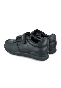 Zapatos de cuero negros con una textura suave, punta redonda y correa de velcro. Presentan perforaciones en la punta y una marca en el talón.