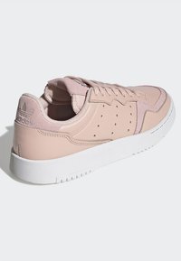Zapatilla de cuero rosa claro con suela de goma blanca. Presenta detalles de costura, diseño con cordones y pequeñas perforaciones para transpirabilidad.