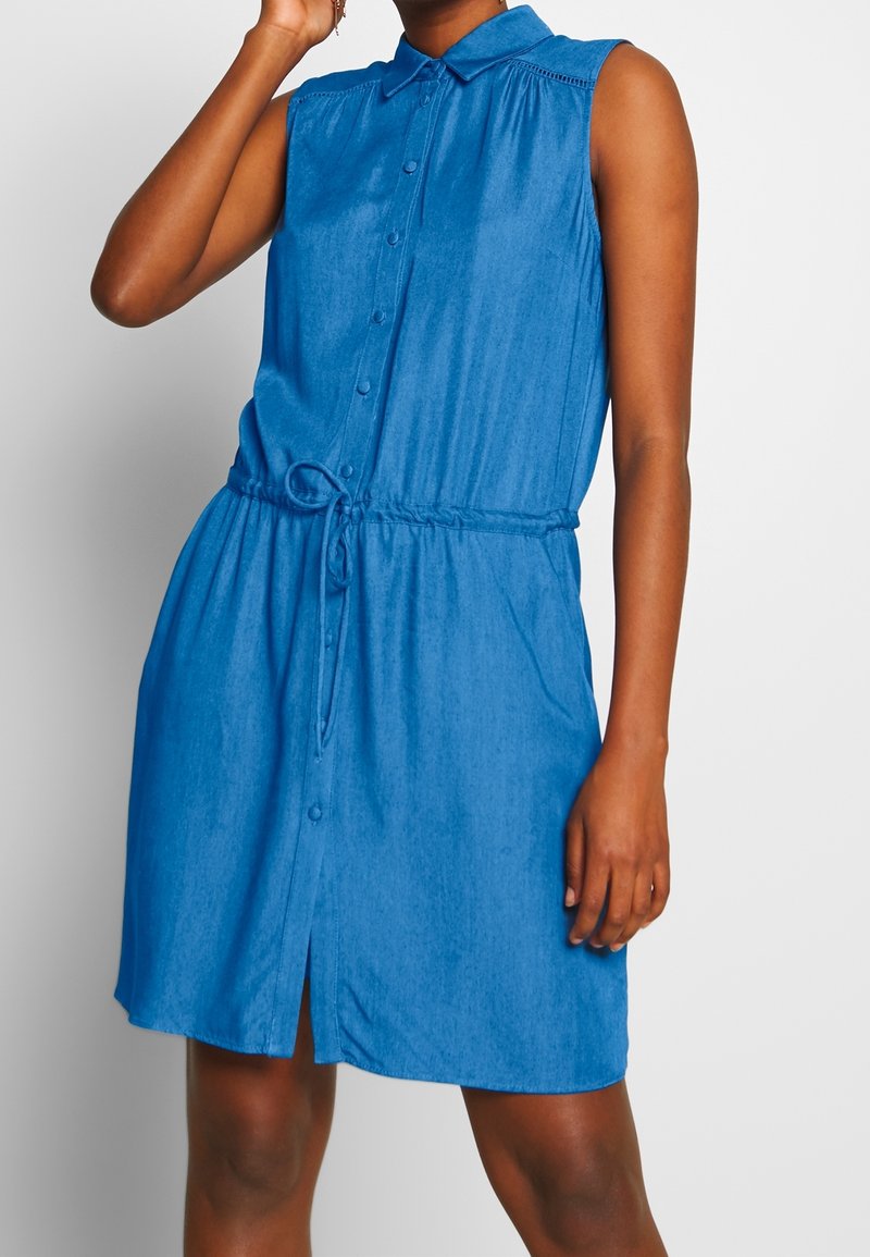 Robe sans manches bleu avec un col, un devant à boutons, une taille à cordon ajustable et un ourlet légèrement évasé. Texture de tissu lisse.