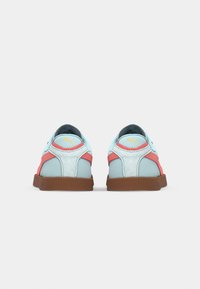 Chaussures de sport bleu clair et corail avec une finition en cuir lisse, un col rembourré et une semelle en caoutchouc marron. Elles présentent un logo jaune sur le talon.