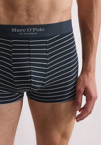 Boxer ajustados a rayas marino en tejido suave con una banda oscura que presenta el logo de "Marc O'Polo". Rayas horizontales blancas a lo largo del material.