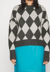 Maglione lavorato a maglia con un motivo a rombi grigio e bianco, maniche lunghe e scollatura rotonda a coste. Abbinato a una gonna turchese uniforme.