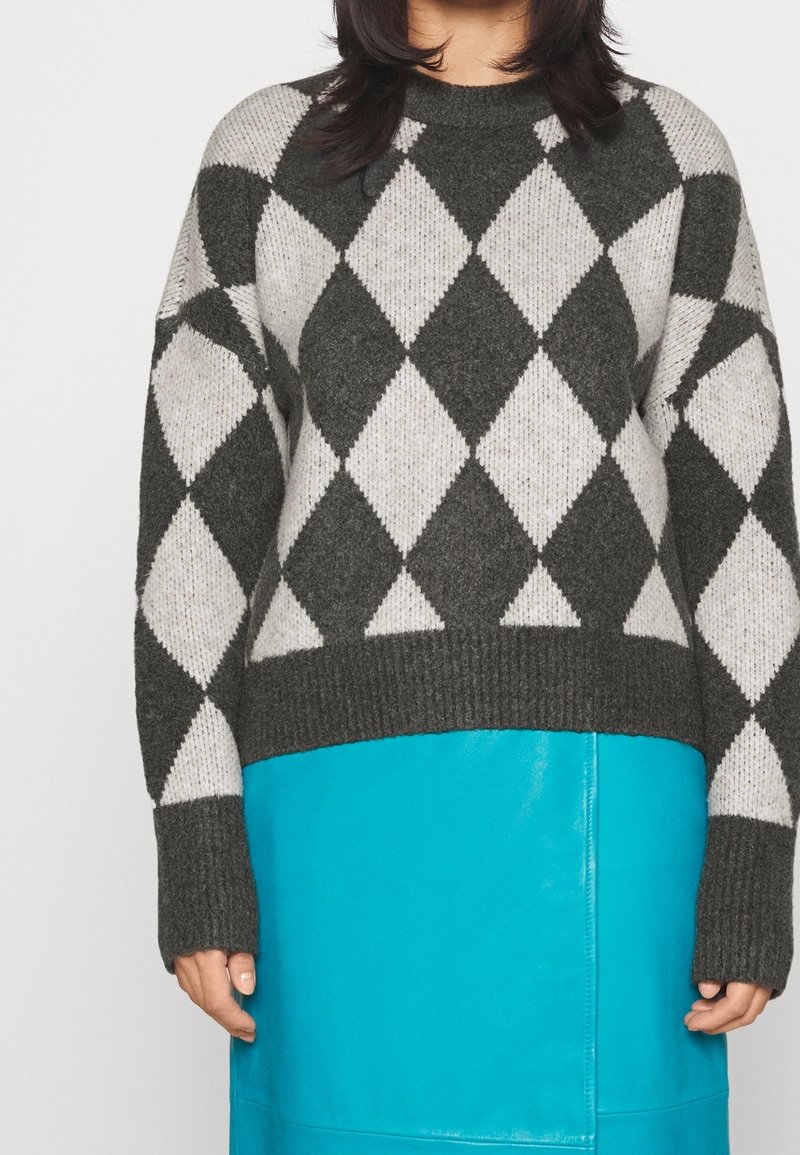 Maglione lavorato a maglia con un motivo a rombi grigio e bianco, maniche lunghe e scollatura rotonda a coste. Abbinato a una gonna turchese uniforme.