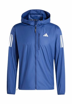 Blauwe lichte capuchonjas met ritssluiting aan de voorkant, borstzak met rits en wit drie-strepenlogo op mouwen en borst.