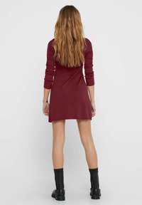 Robe en tricot bordeaux avec une texture côtelée, manches longues, ourlet évasé, associée à des bottines noires.