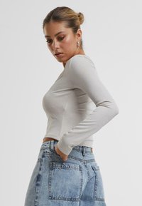 Lyse grå langermet topp laget av et teksturert stoff med en lett glans, kombinert med høytlivede blå denimjeans med baklommer.