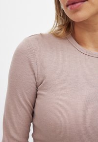 Long-sleeve, ribbed top in soft mauve fabric with a round neckline, showcasing a smooth texture and fitted silhouette.