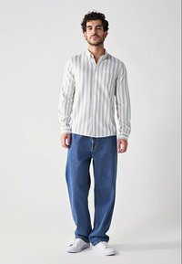 Gestreepte longsleeve shirt in lichtgrijs en wit, gecombineerd met losse blauwe denim jeans en witte sneakers. Opvallende zakdetail op het shirt.