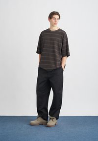Camiseta oversized a rayas marrones con mangas cortas, combinada con pantalones de pierna ancha negros y botas gris claro con cordones y suela resistente.