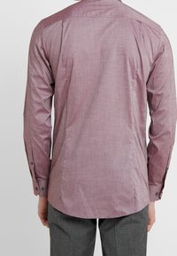 Camisa de manga larga y cuello en tejido rosa claro con una textura sutil. Presenta puños con botones y detalle en el hombro, estrechándose en la cintura.