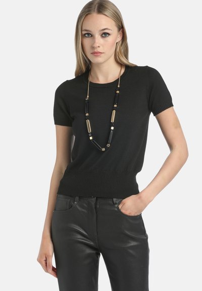 Juodas megztinis trumpomis rankovėmis su prigludusia juosmeniu. Derinamas su juodomis odinėmis kelnėmis. Papuoštas ilga grandinėle su auksiniais ir juodais akcentais.