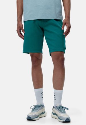Teal treningsshorts med en glatt tekstur, med en klassisk passform og sidelommer, kombinert med lyseblå sneakers og hvite ankelsokker.