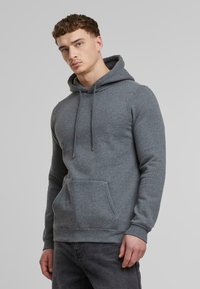 Felpa grigia in misto cotone, con cappuccio regolabile, tasca frontale e polsini a coste. Tessuto liscio con una vestibilità comoda.