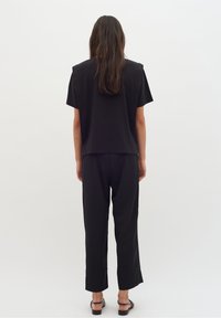 Svart kortärmad topp och lösa svarta byxor, båda med en slät yta. Outfiten har en avslappnad silhuett och minimal design.