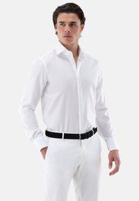 Weißes Hemd mit langen Ärmeln und einem Button-Down-Kragen. Glatter, leichter Stoff, schmale Passform, kombiniert mit einer weißen Hose und einem schwarzen Gürtel.