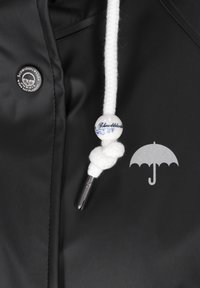 Veste imperméable noire avec un logo d'ombrelle argenté, cordon tressé blanc avec une perle bleue et blanche, et un taquet argenté.