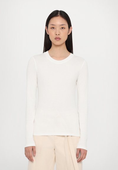 Camiseta blanca de manga larga con un escote redondo, hecha de una tela suave. Combinada con pantalones de color claro y de corte holgado. Diseño sencillo.
