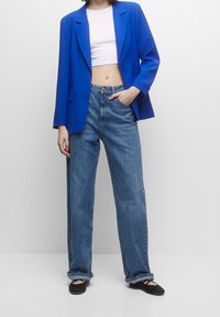 Blaues Blazer mit strukturierten Schultern, verkürztem weißen Oberteil, hochtaillierten blauen Jeans und schwarzen Ballerinas, mit einem lockeren Schnitt und minimalistischem Design.