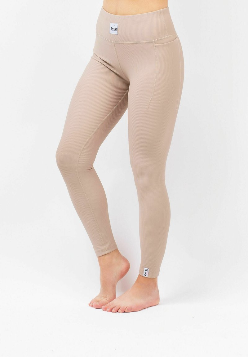 Beige geribde leggings met een hoge tailleband, voorzien van subtiele stikdetails en een klein merketiketje bij de enkel. Zacht, rekbaar materiaal.