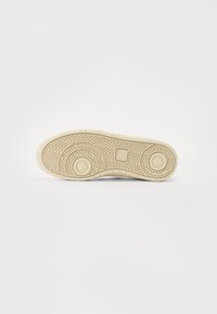 Sole of a shoe, white rubber with curved patterns and circular accents, featuring a textured grip for traction and stability.