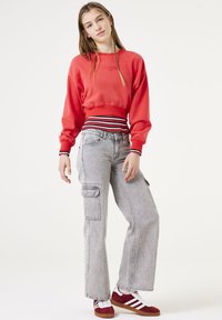 Sudadera recortada roja con dobladillo a rayas, jeans cargo grises con bolsillos y zapatillas rojas con franjas blancas. Diseño simple y ajuste casual.