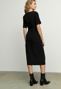 Robe noire midi avec des manches courtes et un col rond, silhouette ajustée, texture lisse, associée à des bottines à talons épais noires.