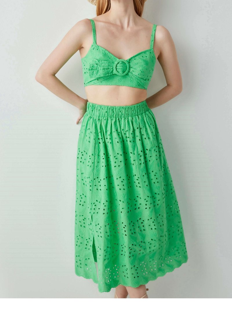 Ensemble vert deux pièces comprenant un crop top ajusté avec un accent circulaire à l'avant et une jupe à volants assortie ornée de broderies ajourées.