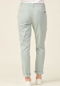 Svetle zelené chinos kalhoty s tapered střihem, ohrnutými manžetami, dvěma zadními kapsami a malou značkovou etiketou na pásu na pravé straně.