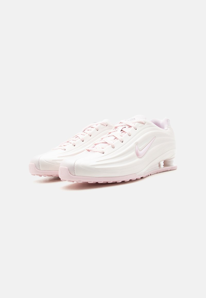 Par de zapatillas Nike blancas y rosa claro con cierre de cordones, diseño ondulado y amortiguación de aire visible en la suela, mostradas sobre un fondo blanco.