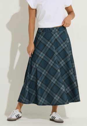 Donna che indossa una maglietta bianca a maniche corte, una gonna midi a quadri blu e neri a linea ad A e sneakers bianche con strisce nere.