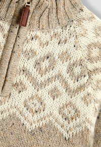 Strickpullover mit hohem Kragen, Halb-Reißverschluss-Design, in Beige mit einer komplizierten gemusterten Textur und Sprenkeln in Braun und Orange.