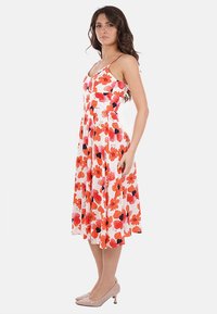 Abito floreale con fiori rossi e arancioni su sfondo bianco; spalline sottili, corpino aderente e gonna svasata alla lunghezza del ginocchio.